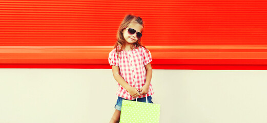Little girl child with shopping bags in the city on red background