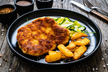 Breaded fried pork chop with sliced cucumbers and french fries on wooden table
