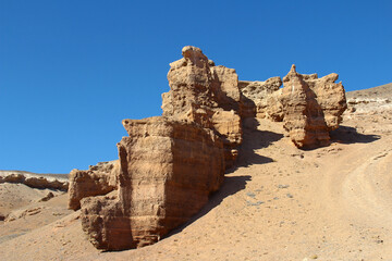 On the sandy slope of a high mountain in the Charyn canyon, a sandy-clay rock with a beautiful relief pattern against a clear sky, summer, sunny