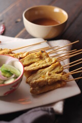 Pork satay served in a white plate with peanut and cucumber dipping sauce.