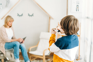 Obraz premium Caucasian school boy kid child taking a photo of his mother mom while she surfing the internet with a tablet. Preschooler playing with camera.