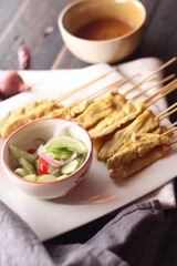 Pork satay served in a white plate with peanut and cucumber dipping sauce.