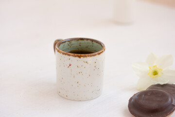 Coffee in white ceramic mug, chocolate cookies, white flowers on white background. Coffee break. in summer,