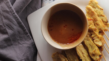 Pork satay served in a white plate with peanut and cucumber dipping sauce.