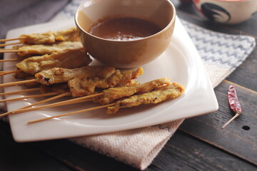 Pork satay served in a white plate with peanut and cucumber dipping sauce.