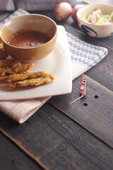 Pork satay served in a white plate with peanut and cucumber dipping sauce.