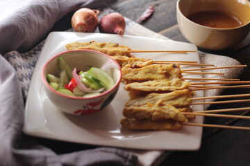 Pork satay served in a white plate with peanut and cucumber dipping sauce.