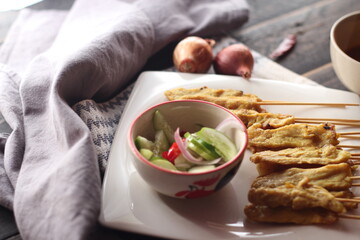 Pork satay served in a white plate with peanut and cucumber dipping sauce.