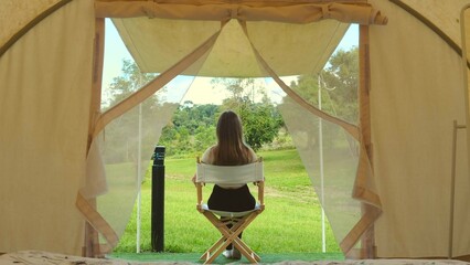 Tourism concept. Back view of travel woman relax outside the modern camp tent. Dawn in a forest with a lonely tent. Camping site, eco tourism concept