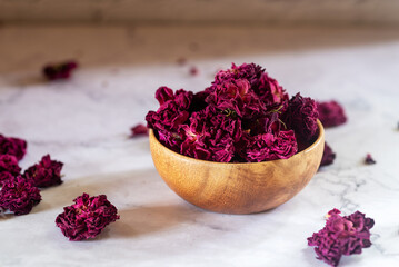 dried organic pink rose buds in wooden bowl on white table.