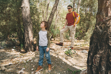 Tourists school boy and his dad walking in the spring forest. Child boy and father wearing casual clothes hiking in summer greenwood leaf forest. Family adventure in the woods.