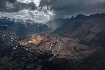 Fotobehang Dramatic view of valley between rocky mountains under overcast sky with sun rays, Caucasus, Russia © Igor