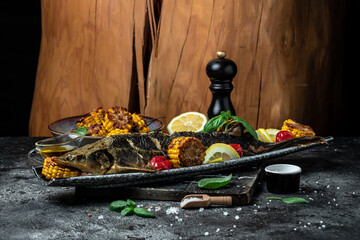 Fototapeta na wymiar Baked fish sturgeon with vegetables and potatoes on dark background. banner, menu, recipe place for text
