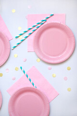 Pink paper disposable plates, napkin and straws for drinks on white background with confetti. Table setting for picnic. Bright eco-court. Birthday, party and holiday concept. Top view, flat lay
