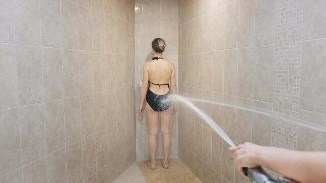 Young woman undergoes Charcot douche in specially equipped bathroom in spa center. Pressurized water jets for anti-cellulite massage backside view