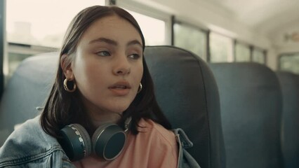 Portrait thoughtful girl sitting bus with headphones. Schoolgirl looking window.