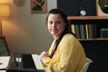 Horizontal medium portrait of modern young female composer with Down syndrome sitting at table with...