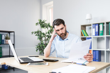 Frustrated and worried businessman looks at bad performance of the company on the documents, an evil man holds in his hands financial reports with errors