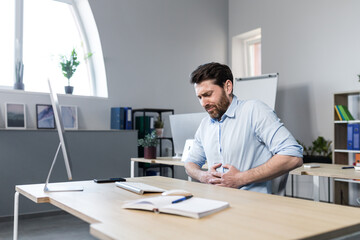 Sick man at work sitting at the table, has severe abdominal pain, businessman unhappy and upset