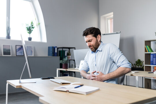 Sick Man At Work Sitting At The Table, Has Severe Abdominal Pain, Businessman Unhappy And Upset