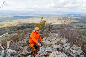 A man in the mountains travels alone, tourist clothes of orange color, a bright jacket from the rain, membrane equipment, trekking in the mountains.