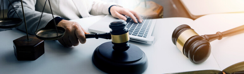 Justice and law concept.Male judge in a courtroom with the gavel, working with, computer and docking keyboard, eyeglasses, on table in morning light