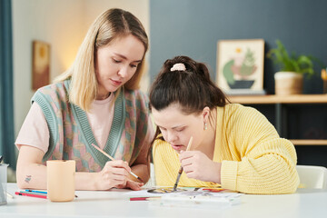 Professional Art teacher having individual class with girl with Down syndrome painting picture with...