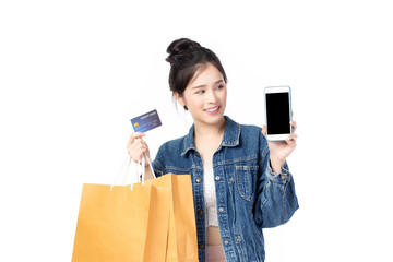 Beautiful Asian stylish young woman in jeans shirt is holding shopping bags, smartphone, credit card and smiling isolated on white background.