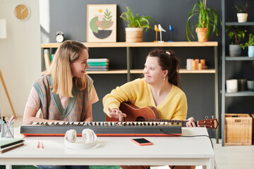Young Caucasian woman sitting next to her female student with Down syndrome teaching her to play...