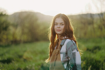Portrait of a young smiling woman in work clothes checkered shirt and apron in nature in the evening after work