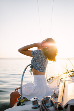 Stylish female tourist resting on yacht and admiring sunset over sea