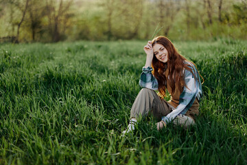 Fototapeta premium A young beautiful woman sits on the green grass in the park and looks out into the setting sun