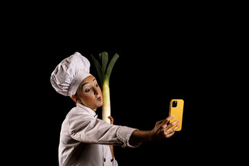 Young female comedian in chef outfit taking selfie with leek