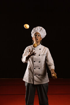 Young female clown chef juggling potatoes in studio