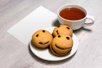 Smile cookies on a white plate with a cup of tea and white paper. Sweet biscuit. Tasty food.
