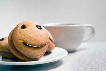 Close-up smile cookies on a white plate with a cup of tea. Sweet biscuit. Tasty food.