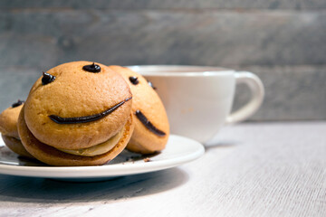 Close-up smile cookies on a white plate with a cup of tea. Sweet biscuit. Tasty food.