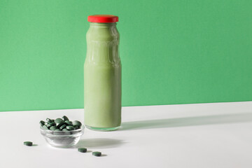 green smoothie in bottle and spirulina algae pills in glass bowl on green, white background.useful habits,self care and healthy lifestyle concept.