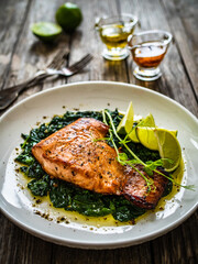 Fried salmon steak with spinach and lime served on wooden table
