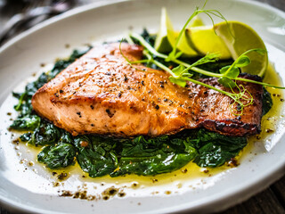 Fried salmon steak with spinach and lime served on wooden table
