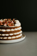 A fig cake with tea leaves in the sponge, lots of whipped cream decoration and fresh sliced figs on top. Gray plate and table, black background. Copy space.