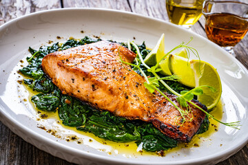 Fried salmon steak with spinach and lime served on wooden table
