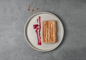 piece of honey cake with strawberry sauce on gray background