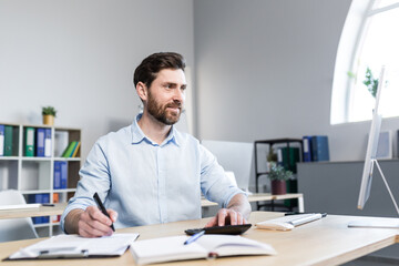 Obraz premium Portrait of a young man. Accountant, economist, financier. Counts on a calculator, sits at a desk at the computer, works with documents