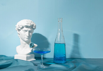 Roman male plaster bust, floral bottle and cocktail glass. Creative arrangement, blue shades.