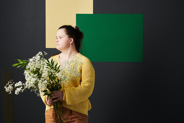 Portrait of young Caucasian model with Down syndrome wearing stylish casual outfit holding bouquet...