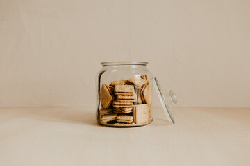 A glass jar of tasty biscuit on wooden table with beige background. Wholemeal cookies for afternoon...