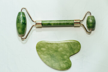 massage stone jade gouache scraper and facial roller light background.