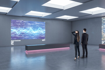 Business people looking at modern digital picture on grey wall in stylish loft interior design exhibition gallery, art investing and NFT concept