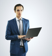 Young businessman in blue suit working with modern laptop, isolated on light grey wall background, closeup